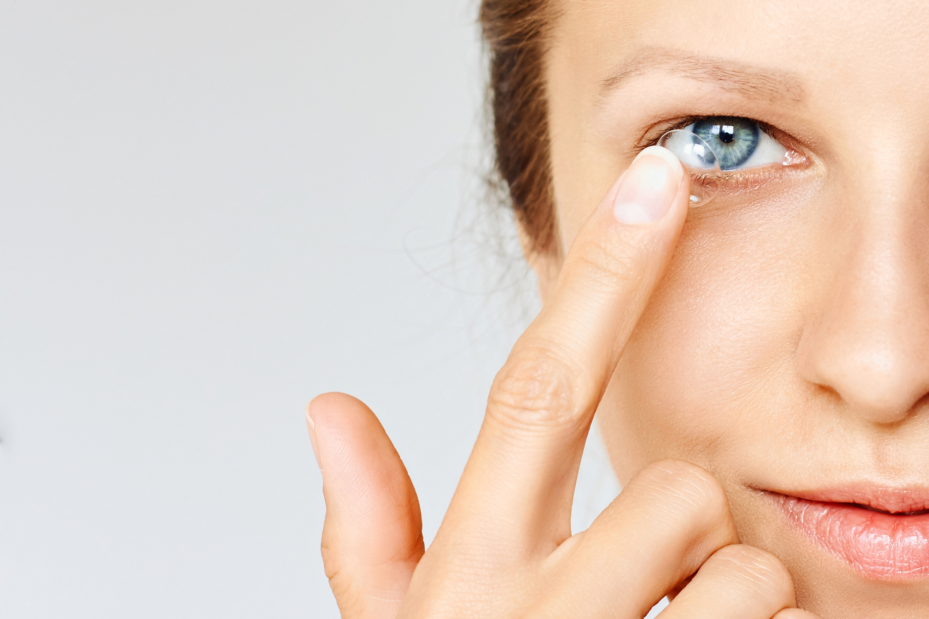 Young woman puts contact lens in her eye.